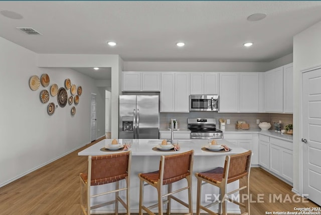 kitchen with a kitchen breakfast bar, backsplash, visible vents, appliances with stainless steel finishes, and light wood-style floors