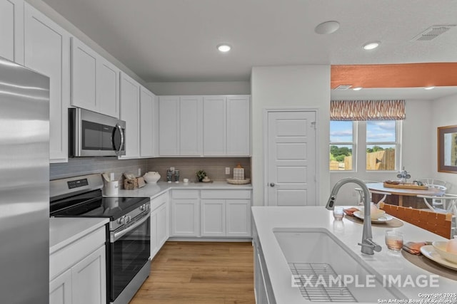kitchen featuring white cabinets, appliances with stainless steel finishes, light countertops, decorative backsplash, and visible vents