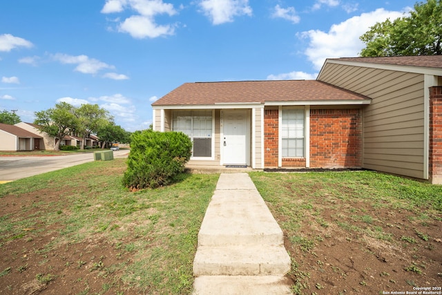 view of front facade featuring brick siding, a front yard, and roof with shingles