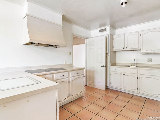 kitchen with wall chimney range hood, visible vents, a sink, black electric stovetop, and white cabinetry