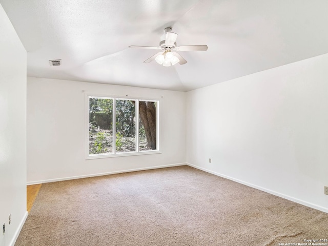 carpeted empty room with baseboards, ceiling fan, vaulted ceiling, and visible vents