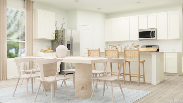 kitchen with decorative backsplash, a kitchen breakfast bar, white cabinetry, light wood finished floors, and stainless steel appliances