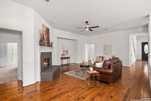 living area featuring ceiling fan, a fireplace, wood-type flooring, arched walkways, and visible vents
