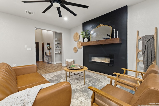 living room with a ceiling fan, visible vents, a large fireplace, wood finished floors, and baseboards
