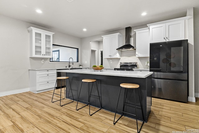 kitchen featuring a breakfast bar area, wall chimney exhaust hood, a center island, stainless steel appliances, and white cabinetry