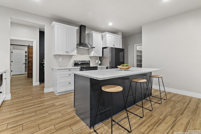 kitchen featuring appliances with stainless steel finishes, a breakfast bar area, light wood-style flooring, wall chimney exhaust hood, and white cabinetry