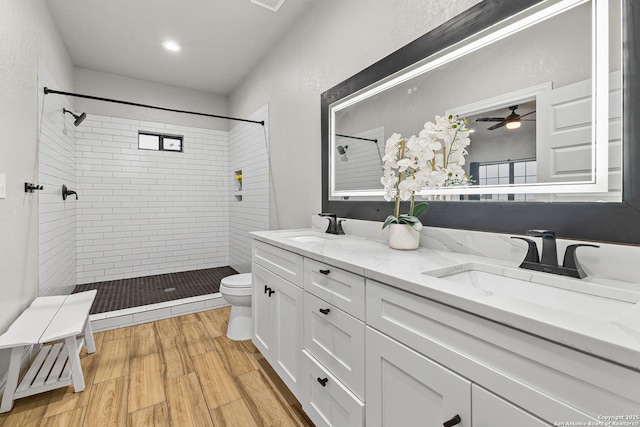 bathroom featuring a sink, a tile shower, toilet, and double vanity