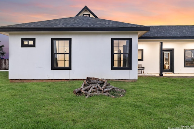 rear view of property featuring a lawn and a shingled roof