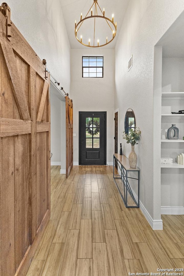 foyer with an inviting chandelier, visible vents, wood finished floors, baseboards, and a barn door