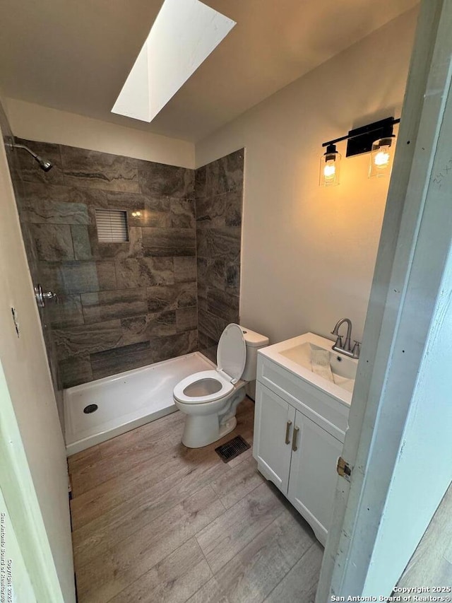 bathroom featuring vanity, toilet, tiled shower, and wood finished floors
