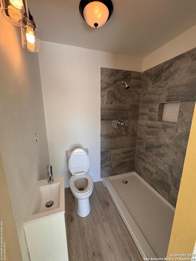bathroom featuring wood finished floors, a tile shower, and toilet