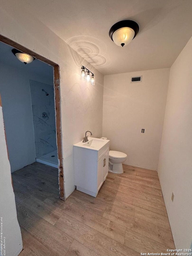bathroom featuring visible vents, vanity, wood finished floors, toilet, and a stall shower
