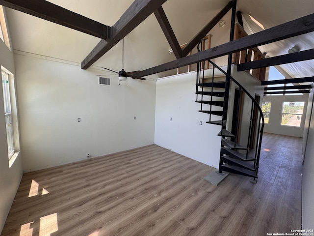 unfurnished living room with beam ceiling, wood finished floors, ceiling fan, high vaulted ceiling, and stairway