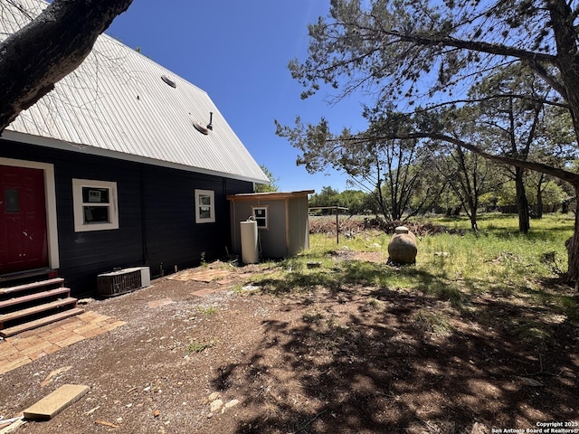 view of side of property with entry steps, cooling unit, and metal roof