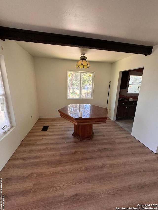 unfurnished dining area featuring visible vents, wood finished floors, and beamed ceiling