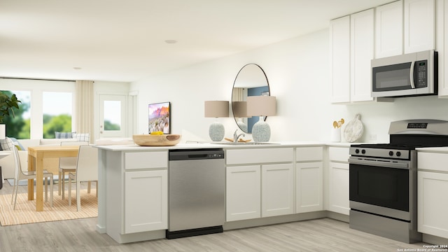 kitchen with appliances with stainless steel finishes, a sink, a peninsula, white cabinetry, and light wood-type flooring