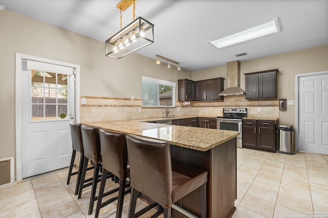 kitchen with stainless steel range with electric stovetop, a peninsula, light tile patterned flooring, a breakfast bar area, and wall chimney range hood