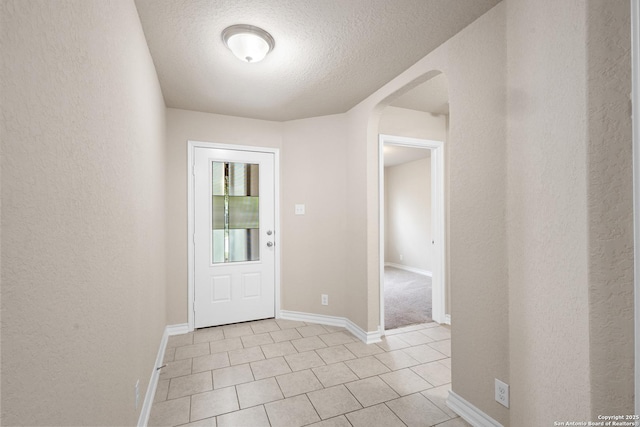 foyer entrance featuring a textured wall, baseboards, a textured ceiling, arched walkways, and light tile patterned floors