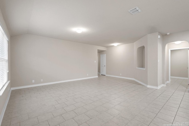 spare room featuring arched walkways, baseboards, vaulted ceiling, and visible vents