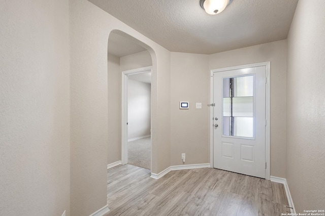 entryway featuring light wood-type flooring, arched walkways, a textured ceiling, and baseboards