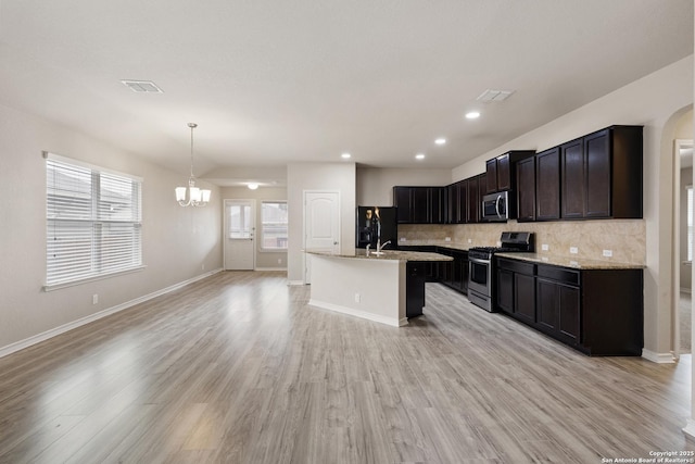 kitchen featuring an inviting chandelier, decorative backsplash, open floor plan, light wood finished floors, and stainless steel appliances