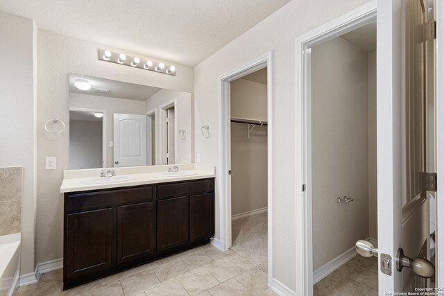 bathroom with double vanity, a walk in closet, a sink, and tile patterned floors