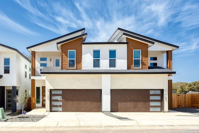 modern home featuring concrete driveway, an attached garage, fence, and stucco siding