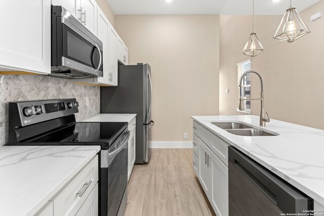 kitchen featuring baseboards, white cabinets, a sink, light wood finished floors, and appliances with stainless steel finishes