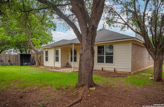 back of property featuring a yard, a patio, fence, and roof with shingles