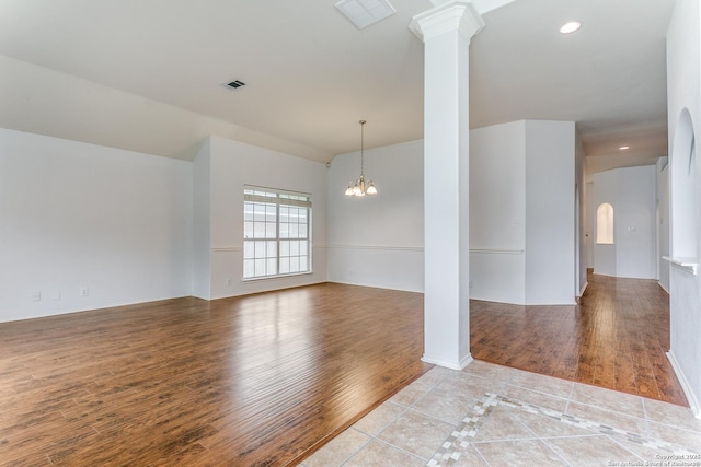 spare room with visible vents, wood finished floors, and a notable chandelier