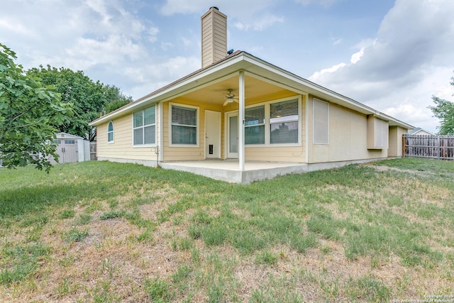 back of property with fence, a patio, a shed, a ceiling fan, and a lawn