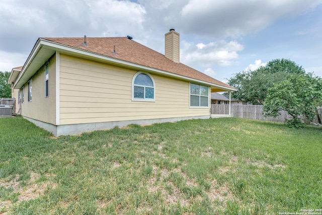 back of house featuring a lawn, fence, a chimney, and central AC unit