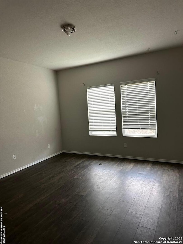 unfurnished room featuring baseboards and dark wood-style flooring