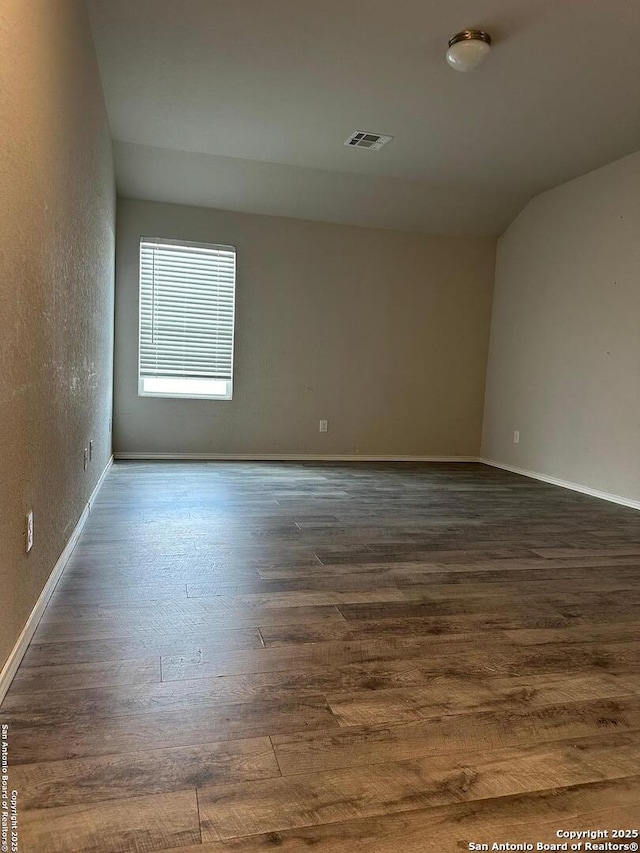 unfurnished room with a textured wall, baseboards, vaulted ceiling, dark wood-type flooring, and visible vents