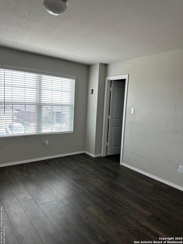 unfurnished room with baseboards, a textured ceiling, and dark wood-style floors