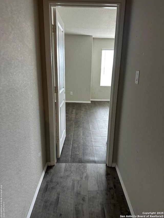 hallway featuring baseboards and dark wood-type flooring