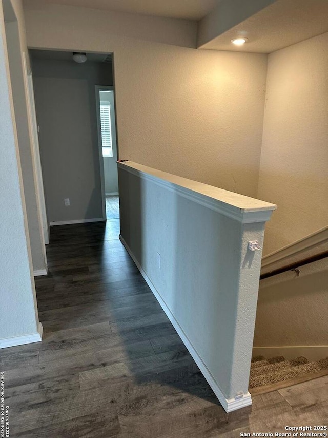 hall with dark wood-type flooring, baseboards, and a textured wall