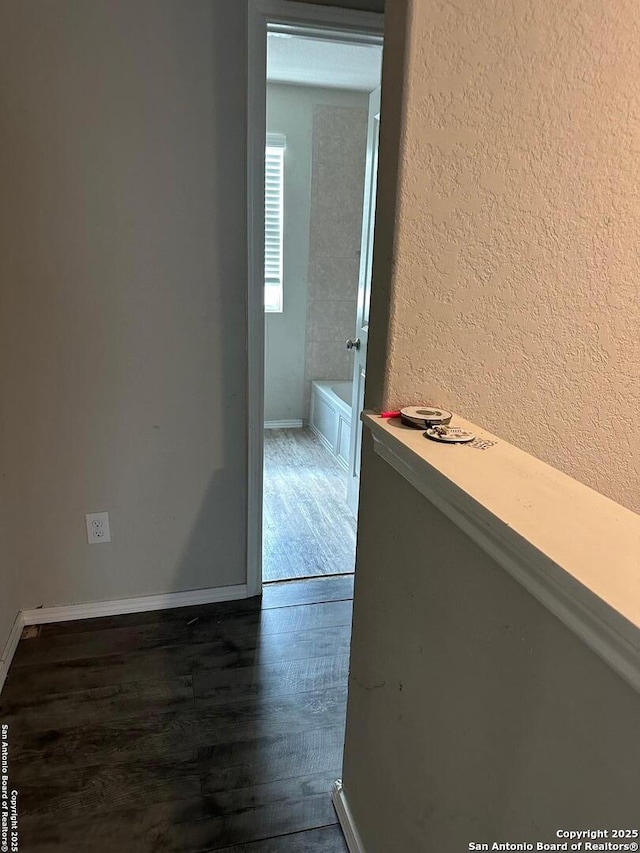 corridor featuring baseboards, a textured wall, and wood finished floors