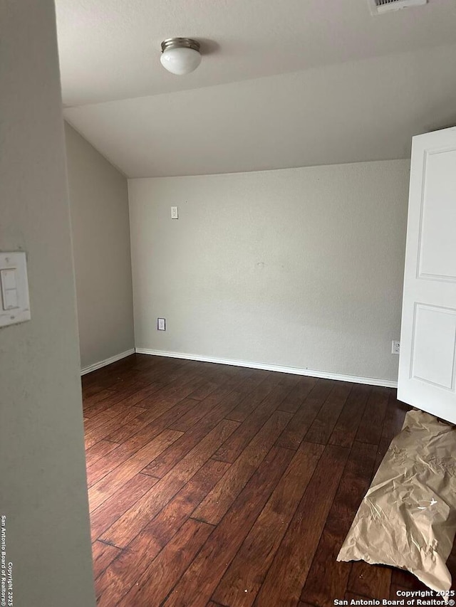 empty room with dark wood-type flooring, baseboards, and lofted ceiling