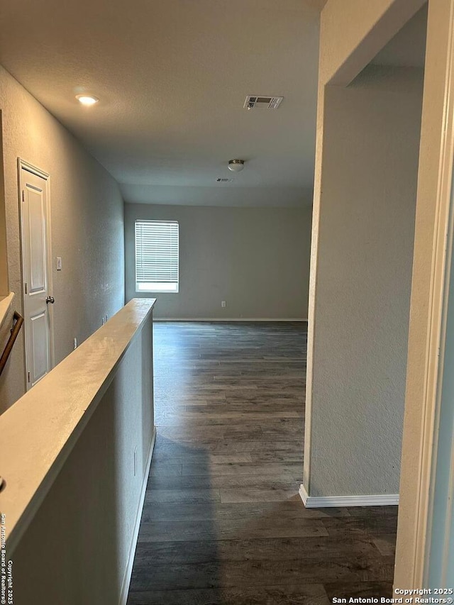 hall featuring visible vents, a textured wall, baseboards, and dark wood-style floors