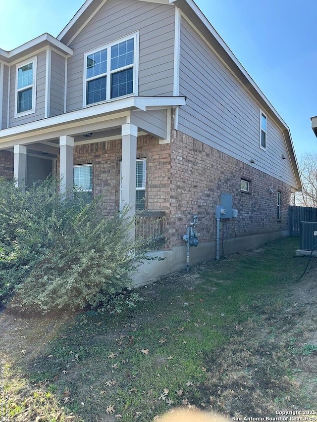 view of side of property with a yard, brick siding, and central AC