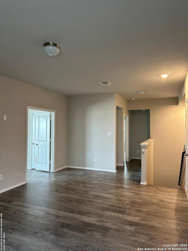 unfurnished room featuring dark wood-type flooring, baseboards, and visible vents