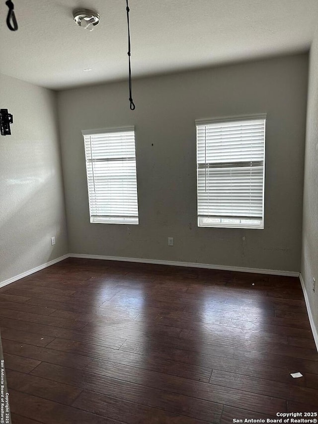 spare room featuring baseboards and dark wood-style flooring