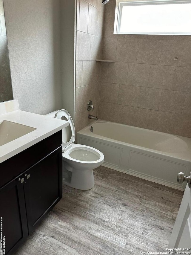 bathroom with a textured wall, vanity, toilet, wood finished floors, and shower / bathing tub combination