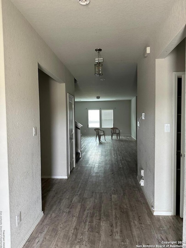 hallway with baseboards, a textured wall, and dark wood finished floors