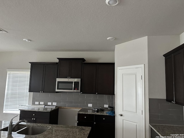 kitchen with stainless steel microwave, light stone countertops, a sink, and tasteful backsplash