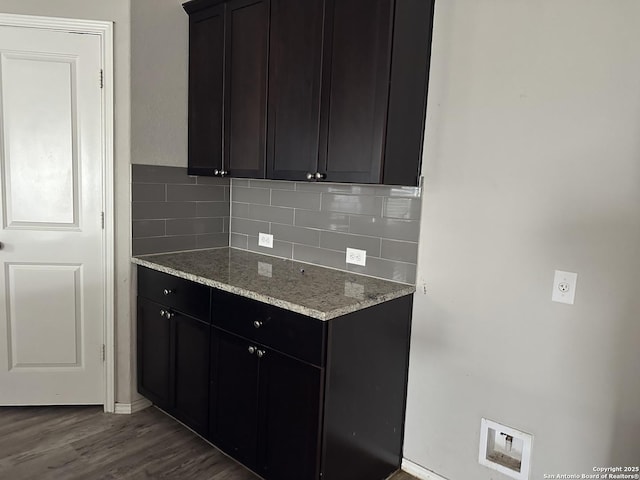 kitchen with dark wood-style flooring, light stone countertops, dark cabinetry, baseboards, and backsplash