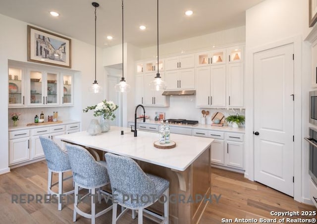kitchen with a sink, a kitchen breakfast bar, white cabinetry, stainless steel gas stovetop, and under cabinet range hood