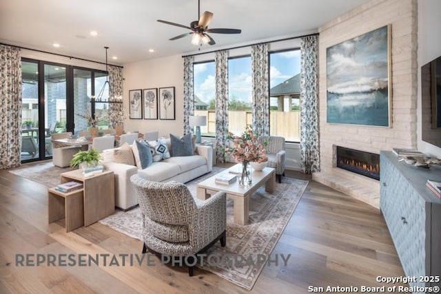 living area with recessed lighting, ceiling fan with notable chandelier, wood finished floors, and a fireplace
