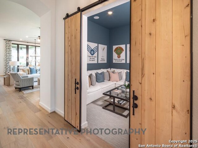 corridor with arched walkways, baseboards, a barn door, and wood finished floors